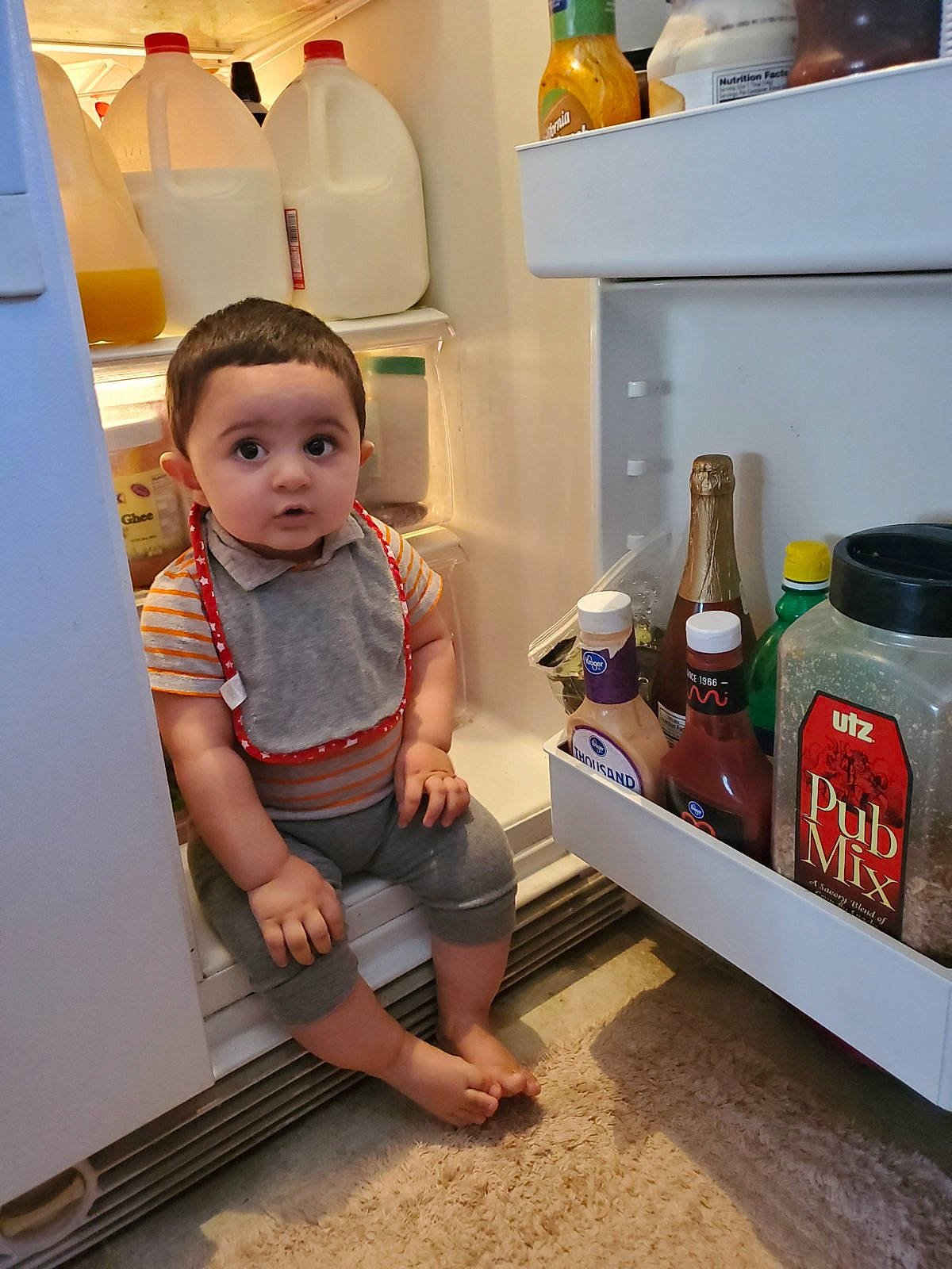 Mustafa joined the competition — help win amazing prizes! baby, baby_toddler_clothing, bottle, carbonated_soft_drinks, child, drink, flooring, gas, home_appliance, kitchen_appliance, machine, orange, person, plastic_bottle, refrigerator, room, shelf, shorts, surprise, t_shirt