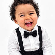 Matthew is registered to the contest to win money with this photo: child, toddler, portrait, smiling, laughing, curly_hair, formalwear, bow_tie, suspenders, white_shirt, black_clothing, studio, indoor, seated, happy, face, eyes, teeth, close_up, photography