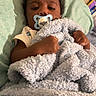 baby, bed, blanket, child, clothing, comfort, curly_hair, furniture, hand, indoors, infant, lying_down, pacifier, person, portrait, resting, sleepwear, soft_texture, toddler, young_child