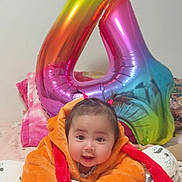 Isabella Grace is registered to the contest to win money with this photo: baby, child, smiling, orange_jacket, pigtails, bed, blanket, pillow, balloon, number_four, rainbow_colors, indoor, cute, happy, person, cozy, soft_toys, pink_bedspread, home, portrait