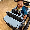 Zaedyn joined the competition — help win amazing prizes! baby, child, toy_car, smile, indoor, floor, curly_hair, bib, blue_clothing, steering_wheel, kitchen, cabinet, footwear, happy, play, person, infant, seat, toy, face