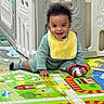 baby, child, smiling, playmat, crawling, curly_hair, bib, socks, indoor, playpen, colorful, floor, cute, happy, person, toddler, toy, home, young_child, fun