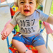 Lyndon joined the competition — help win amazing prizes! toddler, child, smiling, curly_hair, shirt, shorts, bracelet, chair, outdoor, daylight, happy, person, colorful, playful, expression, cute, sitting, casual_clothing, sunlight, face