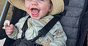 Atlas is registered to the contest to win money with this photo: baby, smiling, stroller, hat, onesie, child, happy, outdoor, plush_toy, seatbelt, infant, cute, playful, joyful, clothing, person, face, headwear, sitting, fun