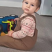 Ianis Matthias joined the competition — help win amazing prizes! toddler, child, baby, carpet, toy, overalls, long_sleeve_shirt, indoor, floor, person, young_child, curious, sitting, carpeted_floor, play, looking, brown_clothing, patterned_shirt, toy_vehicle, door