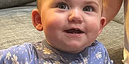 Katherine is registered to the contest to win money with this photo: baby, child, infant, smiling, blue_onesie, floral_pattern, couch, gray_couch, indoor, happy, face, eyes, curious, person, cute, young_child, home, casual, portrait, playful