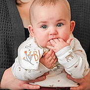 Katherine is registered to the contest to win money with this photo: baby, infant, child, hands, fingers, face, eyes, clothing, sweater, adult, holding, cute, portrait, closeup, indoor, person, comfort, nibbling, expression, soft_light