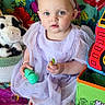 baby, child, girl, lavender_dress, headband, blue_eyes, toy, lollipop, colorful_blanket, floral_pattern, plush_toy, couch, indoor, cute, sitting, portrait, playtime, soft_lighting, expression, infant