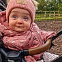 baby, child, stroller, pink_jacket, knit_hat, blue_eyes, outdoor, fall_leaves, cute, drool, polka_dots, warm_clothing, infant, bundle_up, face, expression, person, nature, trees, fence