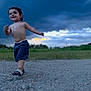 Anthony is registered to the contest to win money with this photo: toddler, child, barefoot, smiling, outdoor, cloudy_sky, grass, rocks, running, happy, nature, evening, curly_hair, blue_shorts, sandals, motion, portrait, candid, sky, field