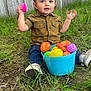 toddler, child, grass, plastic_eggs, bucket, outdoor, fence, shirt, jeans, sneakers, toy, candy, play, happy, nature, spring, easter, curious, sitting, daylight