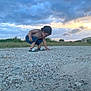 Anthony is registered to the contest to win money with this photo: toddler, child, outdoor, sunset, clouds, gravel, road, grass, shirtless, curly_hair, sandals, nature, sky, exploring, crouching, daylight, young_child, casual, summer, field