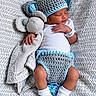 newborn, baby, sleeping, infant, portrait, crocheted_hat, crocheted_diaper_cover, blue, gray, stuffed_elephant, plush_toy, blanket, bed, nursery, cozy, peaceful, white_onesie, socks, patterned_bedding, close_up