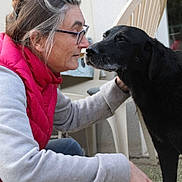 Flickf participe au concours pour gagner de l'argent avec cette photo : woman, dog, black_dog, person, face, glasses, gray_hair, pink_vest, sweater, outdoor, patio, chair, door, window, affection, nose_to_nose, petting, sitting, standing, portrait