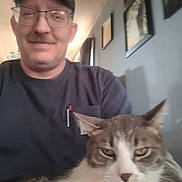 Sammy joined the competition — help win amazing prizes! man, cat, glasses, cap, indoor, portrait, smile, animal, pet, feline, home, wall, picture_frame, casual_clothing, mustache, person, seated, closeup, face, domestic_animal