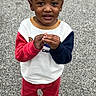toddler, child, curly_hair, pigtails, sweatshirt, red_pants, boots, outdoor, gravel, standing, looking_up, hands_together, casual_clothing, cute, young_child, curious_expression, colorful_clothes, portrait, person, daylight