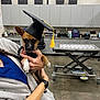 Chloe Anne joined the competition — help win amazing prizes! dog, graduation_cap, person, hand, animal, indoor, cabinet, table, office, clinical, veterinary, floor, watch, clothing, furniture, paper, equipment, holding, brown_dog, small_dog