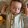 baby, sleeping, striped_shirt, carpet, plush_toy, child, indoors, peaceful, button_up, clothing, young_child, relaxing, cute, portrait, infant, soft_texture, resting, toddler, hands_up, closed_eyes