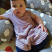 Layla is registered to the contest to win money with this photo: baby, infant, child, headband, bow, striped_dress, leggings, cushion, cloud_pattern, toy, floor, wooden_floor, indoor, person, sitting, tongue_out, cute, chubby_cheeks, comfort, home