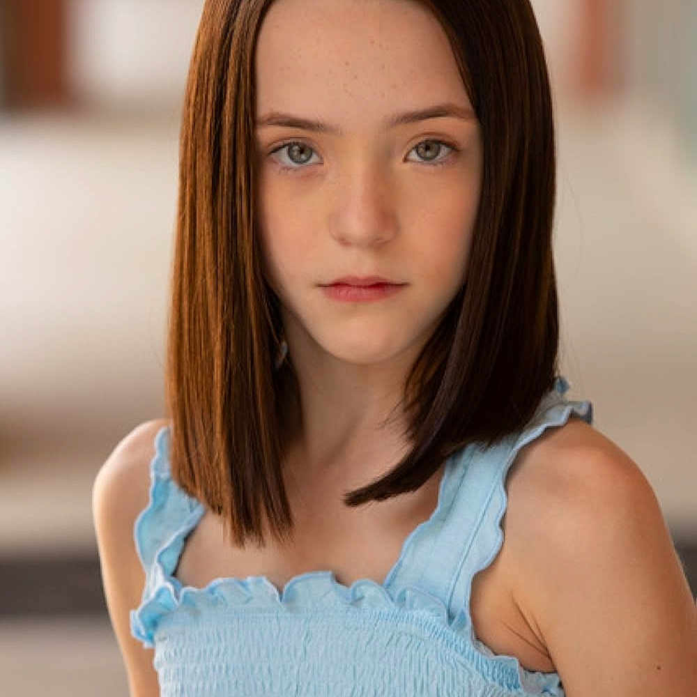 Steven a rejoint le concours — aidez-le/la à gagner de superbes lots ! child, girl, portrait, blue_eyes, brown_hair, straight_hair, light_blue_top, ruffled_clothing, shoulder, skin, face, expression, serene, standing, blurred_background, outdoor, young, person, fashion, head_and_shoulders