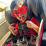 child, car_seat, red_sunglasses, heart_shaped_glasses, tongue_out, red_shirt, chocolate, chocolate_box, seat_belt, car_interior, playful, happy, smiling, person, kid, fun, snack, seat, window, sunlight