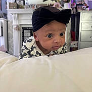 Bobby-Sage is registered to the contest to win money with this photo: baby, infant, headband, black_bow, face, eyes, clothing, white_surface, indoor, room, furniture, decor, flower_vase, photography, portrait, cute, child, young, expression, curious