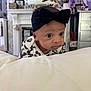 baby, infant, headband, black_bow, face, eyes, clothing, white_surface, indoor, room, furniture, decor, flower_vase, photography, portrait, cute, child, young, expression, curious
