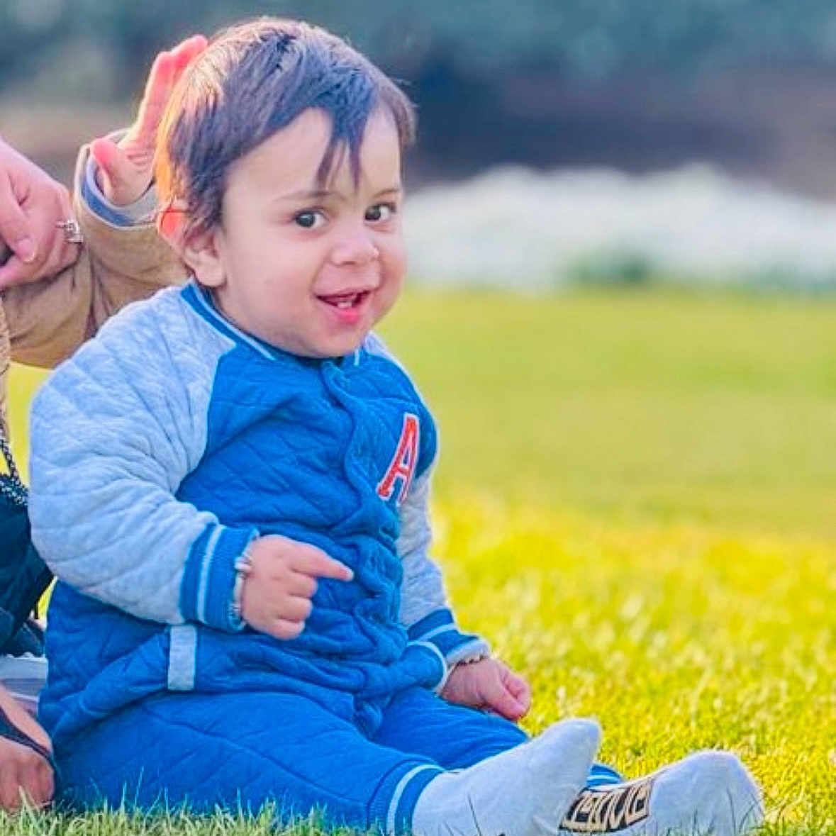 Riyansh joined the competition — help win amazing prizes! blue_clothing, casual_wear, child, daylight, grass, greenery, hand, happy, jacket, nature, outdoor, person, portrait, shoes, sitting, smile, sock, support, toddler, young_child