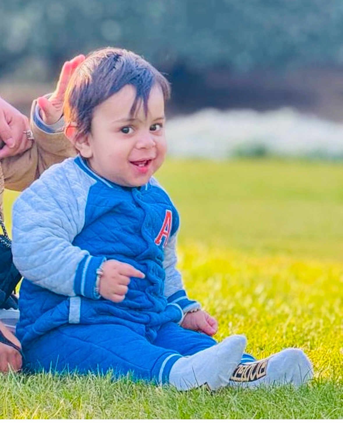 Riyansh joined the competition — help win amazing prizes! toddler, child, grass, blue_clothing, smile, outdoor, person, sitting, happy, casual_wear, daylight, portrait, young_child, jacket, shoes, sock, hand, support, nature, greenery
