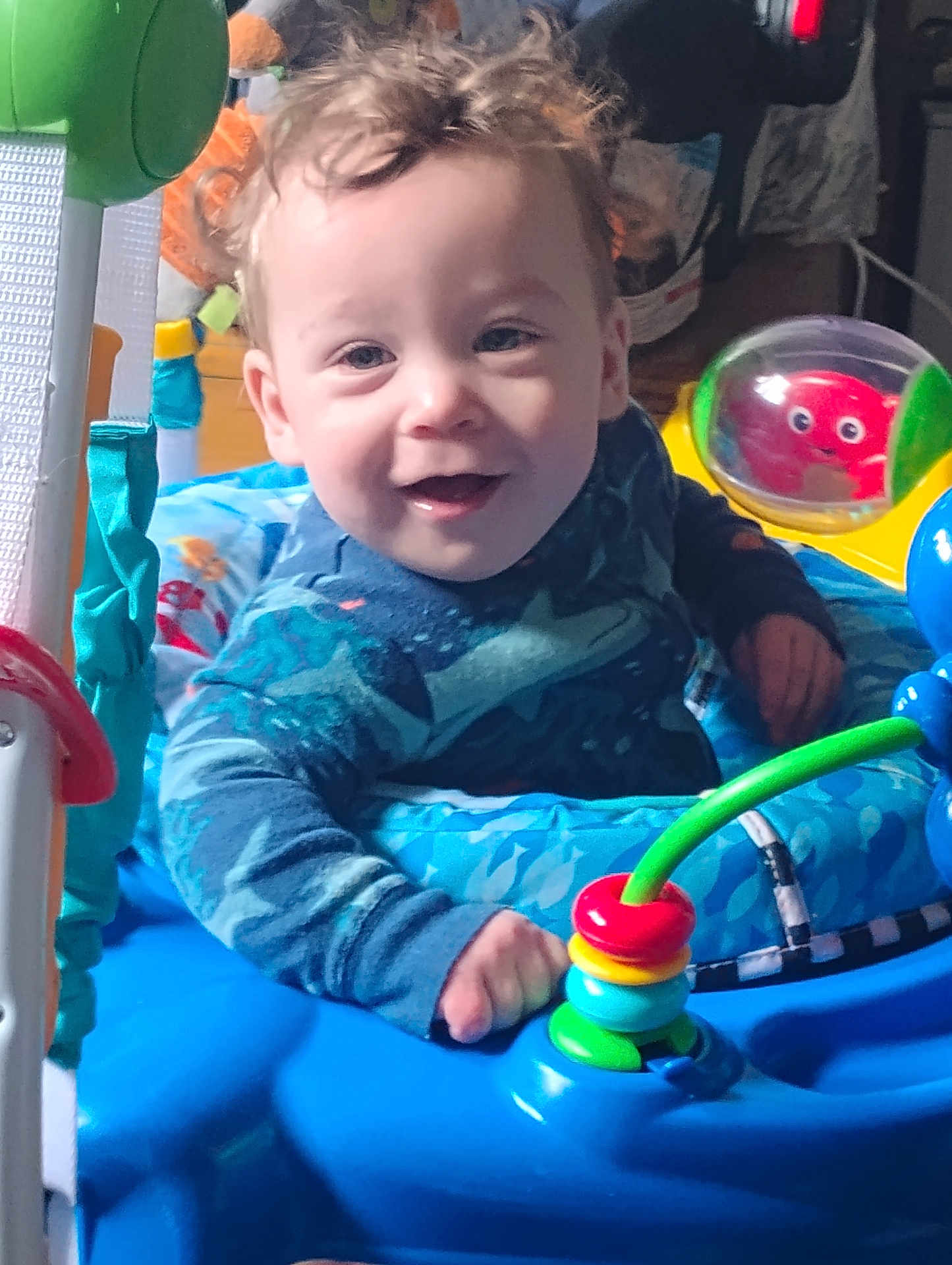 Jaseh is registered to the contest to win money with this photo: baby, child, smiling, curly_hair, blue, toy, activity_center, indoor, playful, colorful, happy, person, infant, cute, face, hand, clothing, seat, bright, fun