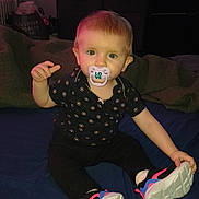 Luna is registered to the contest to win money with this photo: baby, bed, blanket, child, clothing, cozy, cute, footwear, furniture, home, indoor, infant, pacifier, patterned_shirt, person, room, sitting, sneakers, television, young_child