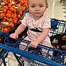 baby, shopping_cart, grocery_store, produce, oranges, child, infant, floor, clothing, socks, person, supermarket, blue, holding, seated, aisle, food, basket, retail, cute