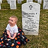 Luna is registered to the contest to win money with this photo: baby, child, blanket, grass, cemetery, gravestone, military_grave, headstone, outdoor, sky, cloudy, rows, memorial, portrait, smile, sitting, person, nature, funny_blanket, veteran