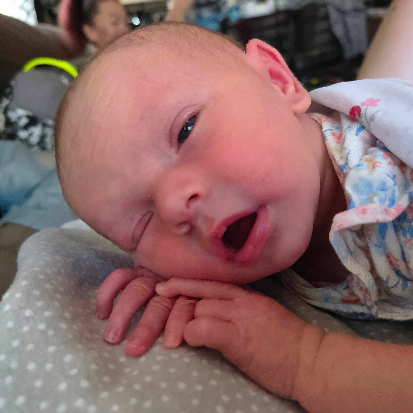 Summer joined the competition — help win amazing prizes! newborn, baby, infant, sleepy, close_up, blanket, floral_outfit, hand, face, mouth_open, eye_half_open, couch, indoor, person_blurred, background_blur, soft_light, skin, head, peaceful, resting