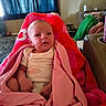 baby, blanket, pink, red, infant, face, tear, indoor, living_room, couch, person, clothing, cozy, curious, child, wrapped, seated, soft, warm, home
