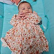 Mia a rejoint le concours — aidez-le/la à gagner de superbes lots ! baby, infant, child, floral_dress, playmat, blue_background, blanket, hands, face, eyes, curious, soft_toys, fabric, clothing, indoor, candid, portrait, lying_down, cute, young_child