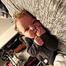 adorable, baby, bed, child, close_up, clothing_rack, cozy, curly_hair, eyes, face, finger_sucking, gray_blanket, gray_clothing, hands, home, indoors, infant, lying_down, portrait, sunlight