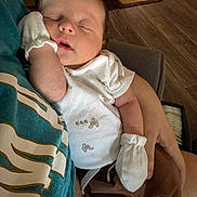 Cohen joined the competition — help win amazing prizes! baby, sleeping, infant, portrait, indoors, person, face, closed_eyes, peaceful, mittens, onesie, blanket, arms, cozy, home, chair, wooden_floor, rug, resting, nap
