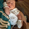baby, sleeping, infant, portrait, indoors, person, face, closed_eyes, peaceful, mittens, onesie, blanket, arms, cozy, home, chair, wooden_floor, rug, resting, nap