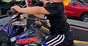 Cohen is registered to the contest to win money with this photo: child, toddler, boy, smiling, portrait, dirt_bike, motorcycle, motocross, outdoor, sunset, golden_hour, vehicle, handlebars, helmetless, black_shirt, shorts, sneakers, parked_cars, street, urban_background
