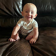 Malcolm is registered to the contest to win money with this photo: baby, child, smiling, sitting, leather_couch, indoor, cute, happy, infant, portrait, home, light, clothing, short_sleeves, skin, face, hands, feet, young, person