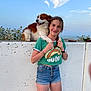 girl, dog, outdoor, sky, clouds, sea, wall, green_shirt, denim_shorts, braid, smile, pet, animal, summer, nature, friendship, happy, leisure, casual, portrait