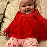 baby, child, smiling, red_dress, pink_headband, bow, heart_pattern, leggings, sofa, cushion, tufted_sofa, indoor, happy, cute, portrait, person, infant, seated, clothing, cozy