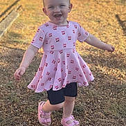 Riley joined the competition — help win amazing prizes! child, toddler, girl, smiling, happy, outdoor, portrait, standing, dress, pink_clothing, hair_bows, sandals, playground, gravel, sunlight, outdoor_photography, fashion, full_body, joyful, background_person