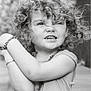 child, curly_hair, black_and_white, portrait, smile, bracelet, tank_top, outdoor, expression, face, person, necklace, cute, young, arms, happy, casual_clothing, closeup, natural_light, playful