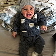 Kamil Alan participe au concours pour gagner de l'argent avec cette photo : baby, child, smiling, happy, sweater, hat, pom_poms, sheep_pattern, couch, blanket, indoor, cozy, clothing, footwear, face, person, portrait, seated, wall, home