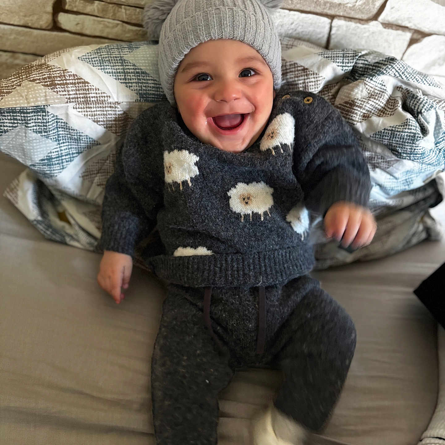 Kamil Alan participe au concours pour gagner de l'argent avec cette photo : baby, blanket, child, clothing, couch, cozy, face, footwear, happy, hat, home, indoor, person, pom_poms, portrait, seated, sheep_pattern, smiling, sweater, wall