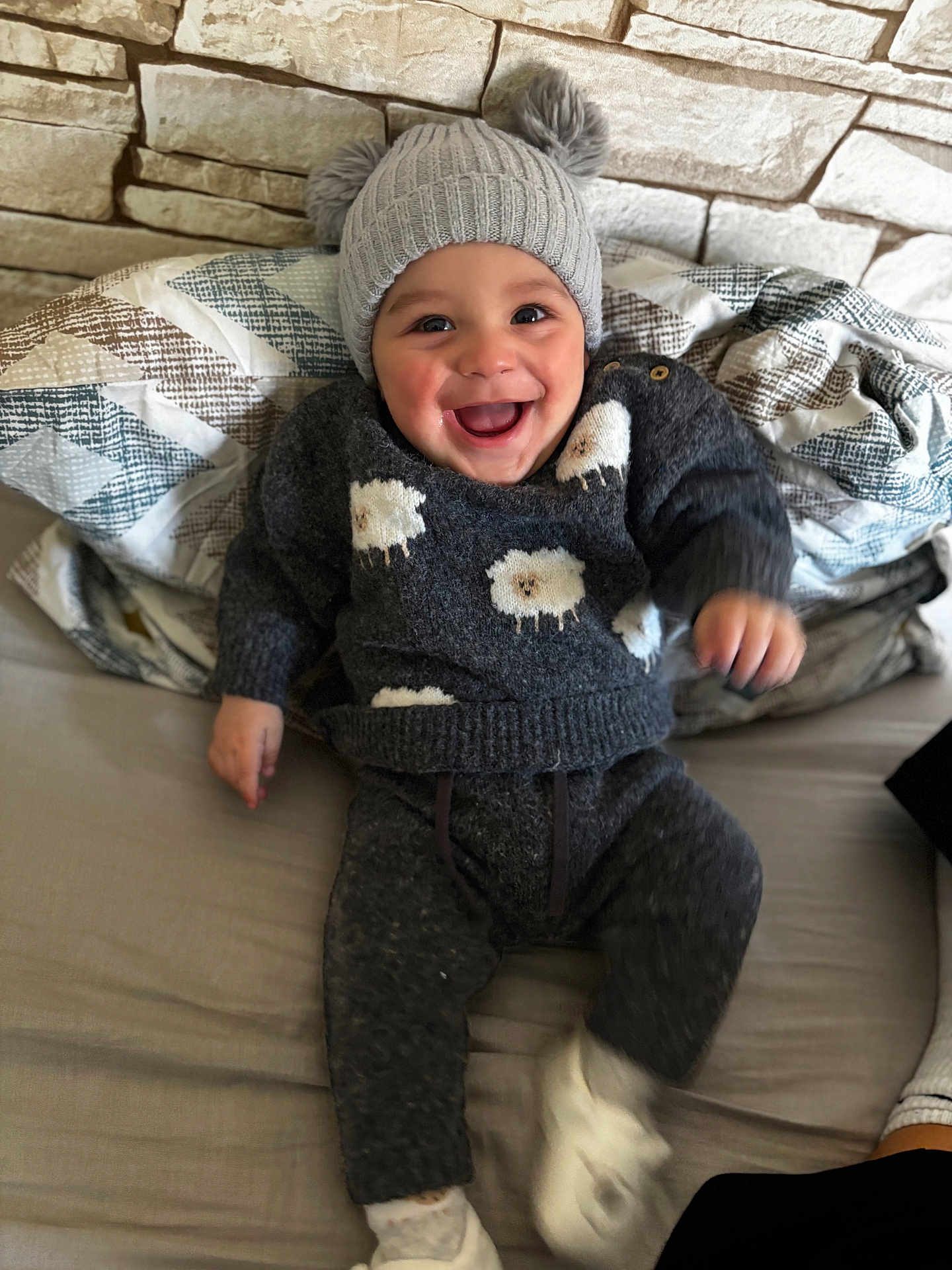 Kamil Alan participe au concours pour gagner de l'argent avec cette photo : baby, child, smiling, happy, sweater, hat, pom_poms, sheep_pattern, couch, blanket, indoor, cozy, clothing, footwear, face, person, portrait, seated, wall, home