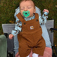 Kane is registered to the contest to win money with this photo: baby, pacifier, sleeping, outdoor, grass, overalls, brown_clothing, person, lap, blue_shirt, socks, stroller, hand, nature, casual, relaxation, infant, quilted, footwear, comfort