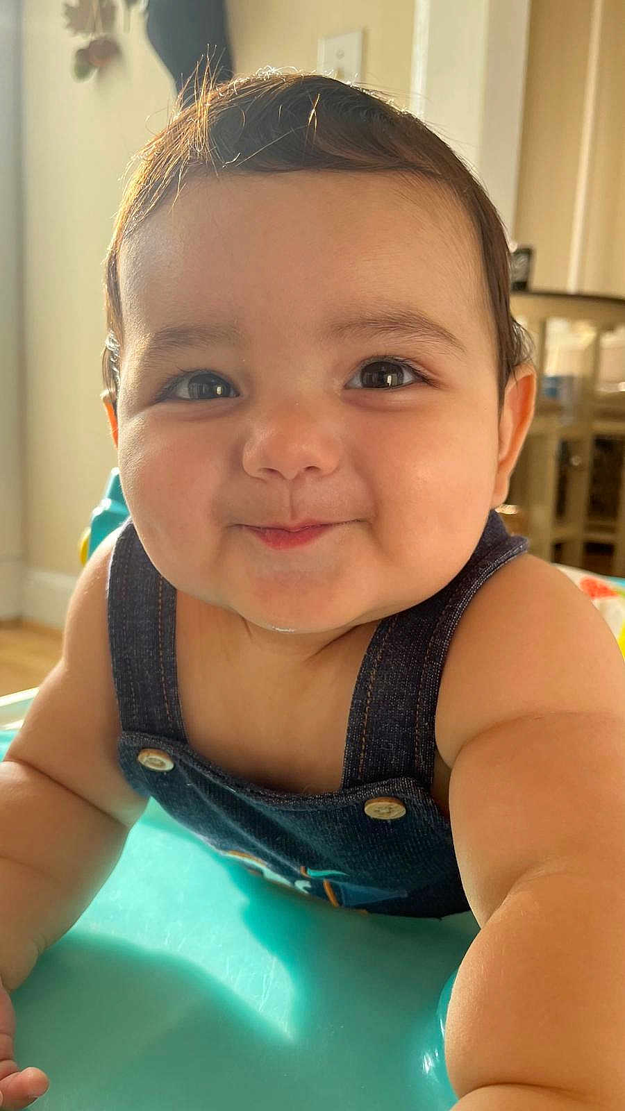 Benjamin is registered to the contest to win money with this photo: baby, child, face, smile, denim, overalls, arm, skin, hair, indoors, furniture, table, light, sunlight, cheeks, eyes, expression, portrait, closeup, cute